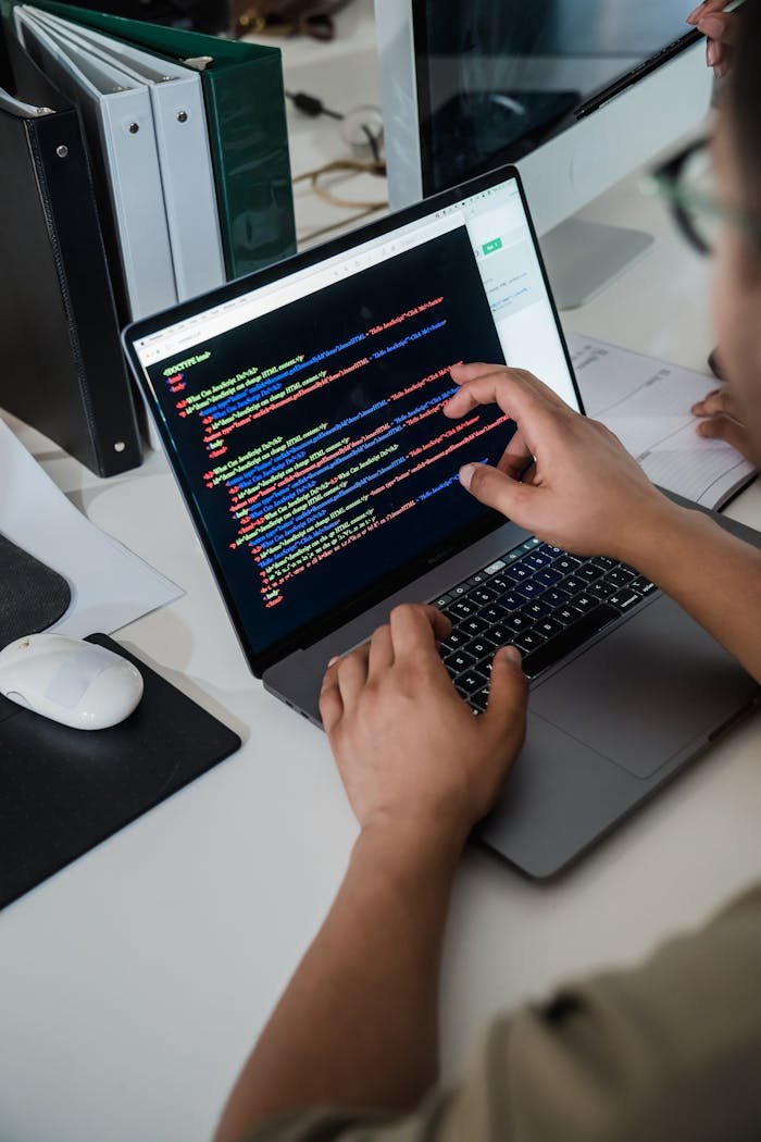 About Close-up of a programmer pointing at a colorful code script on a laptop in an office setting.